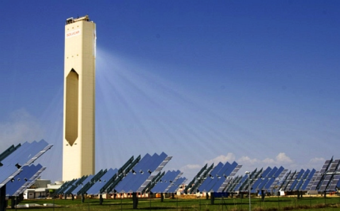 Wavy solar cells in a grassy field with a large white tower behind them. See caption for more info