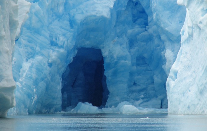 Photograph of an ice cave in a glacier in which the ice is giving off a blue hue.